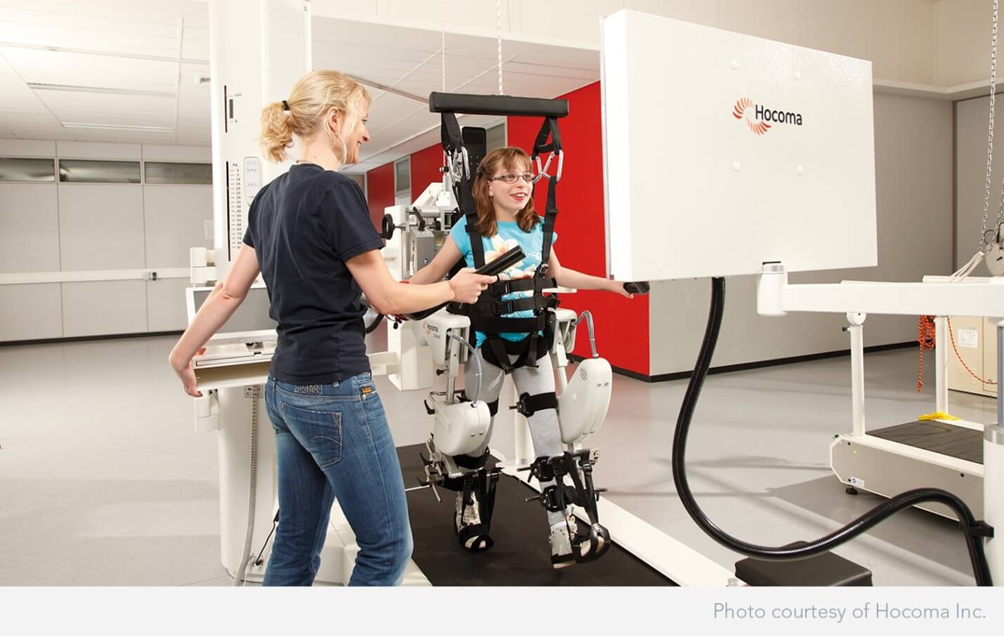 Robotics (1) A woman uses a robotic exoskeleton for assisted walking therapy, guided by a therapist in a clinical setting. The therapist adjusts the device while the user is supported by straps and mechanical aids.