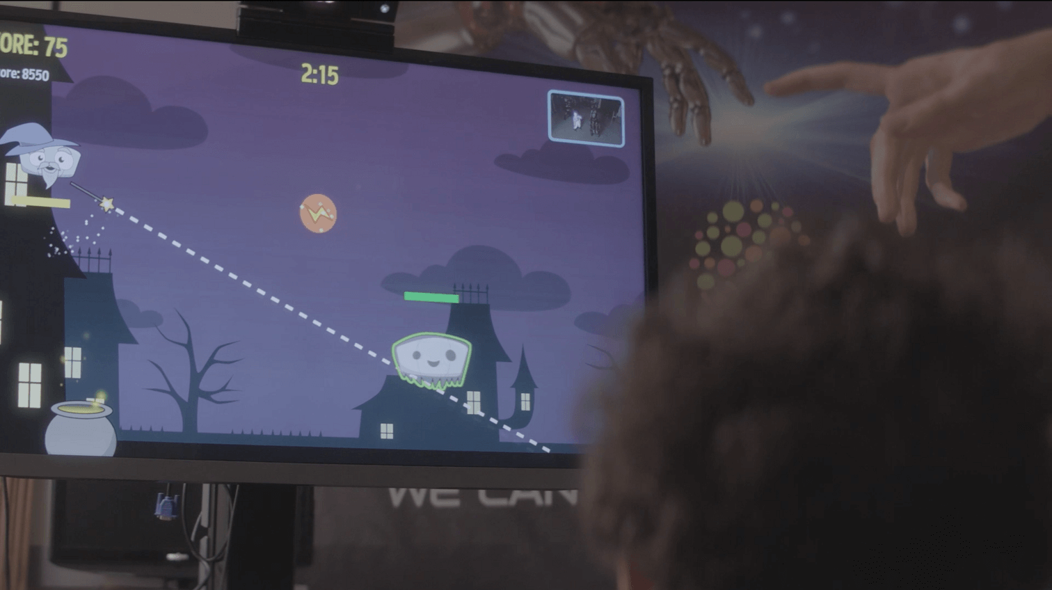 Virtual Reality and Video Games (1) A person points at a computer screen displaying a Halloween-themed game with cartoon ghosts and houses. A score and timer are visible, and a childs head is in the foreground, watching the screen.